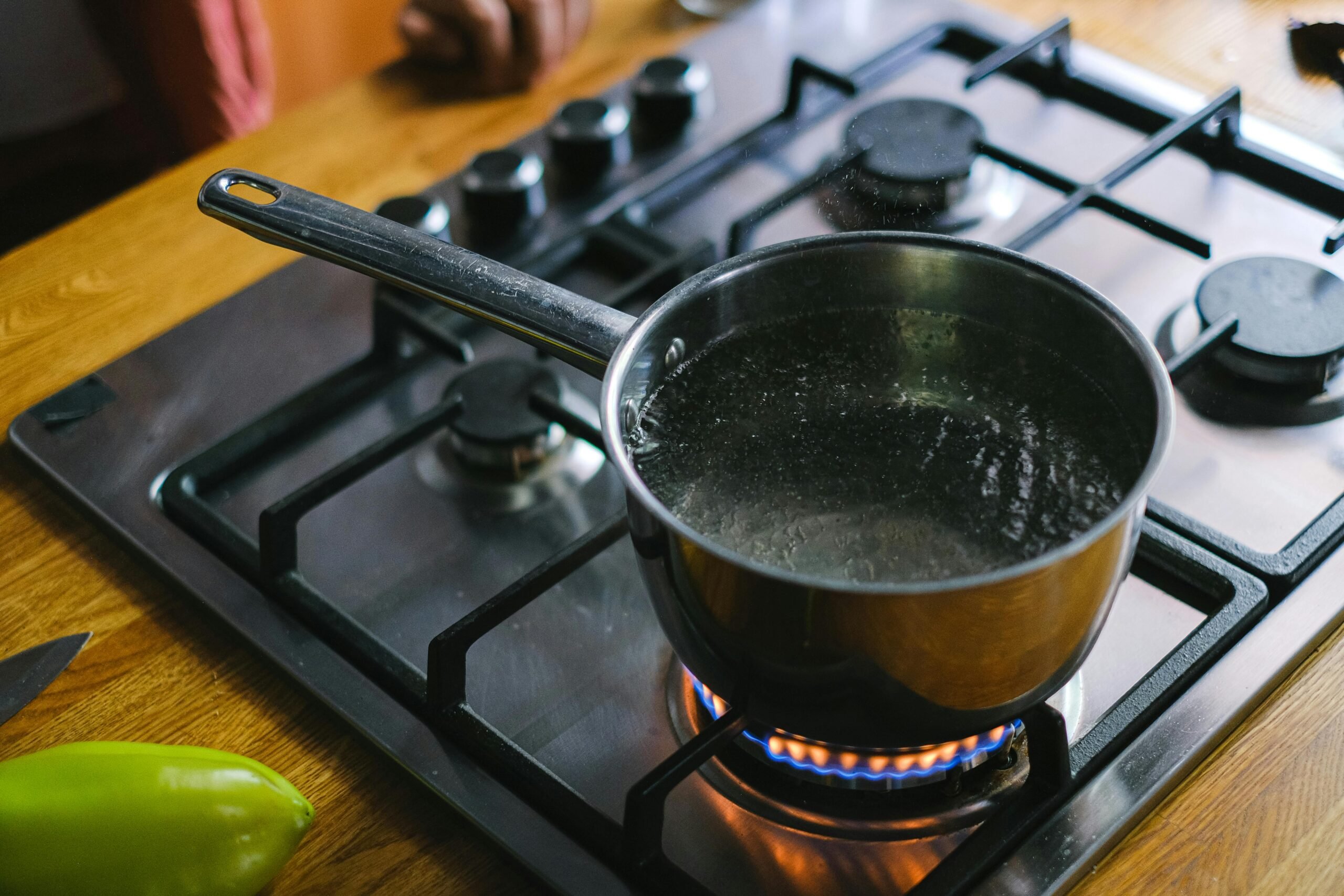 Close-up of boiling water in a stainless steel pot on a gas stove in a kitchen setting.